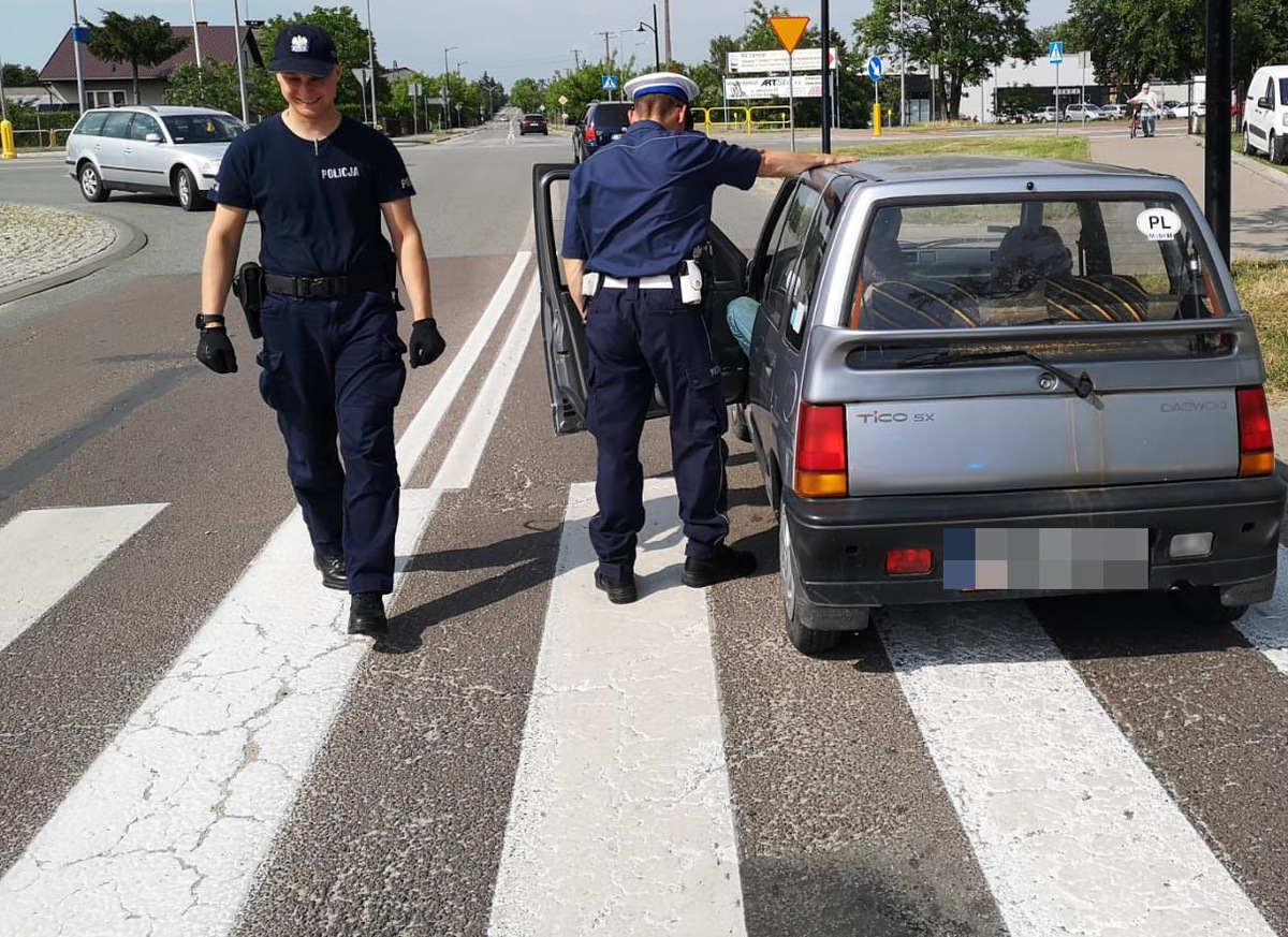 Zdjęcie przedstawia samochód osobowy stojący na przejściu dla pieszych oraz dwóch umundurowanych policjantów.