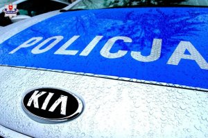 Na obrazku uwidoczniona jest maska pojazdu służbowego Policji marki KIA z napisem na masce Policja