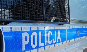 Fragment radiowozu policyjnego - zakratowana szyba i boczny napis na drzwiach Policja