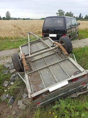 Zdjęcie ilustracyjne przedstawiające pojazd VW koloru czarnego z wywróconą przyczepką samochodową