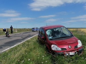 Zdjęcie z miejsca wypadku w Stawkach - rozbite renault, motorower, radiowóz policyjny i policjant ruchu drogowego