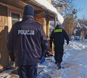 Zdjęcie policjanta kontrolującego pustostan. W tle strażnik miejski