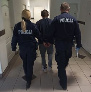 Zdjęcie zatrzymanego prowadzonego przez policjantów w pomieszczeniu