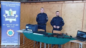 Zdjęcie umundurowanych funkcjonariuszy policji stojących za stanowiskiem wystawowym.