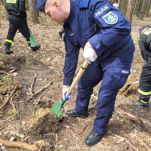 Zdjęcie policjanta w umundurowaniu służbowym koloru niebieskiego trzymającego szpadel