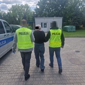 Policjanci w kamizelkach odblaskowych prowadzą zatrzymanego