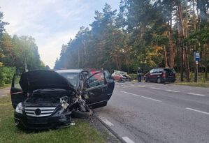 pojazd koloru czarnego z rozbitym przodem. W tle policjant