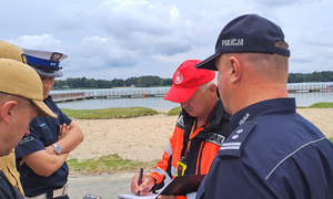 policjanci, strażacy i ratownik wodny rozmawiają w tle jezioro