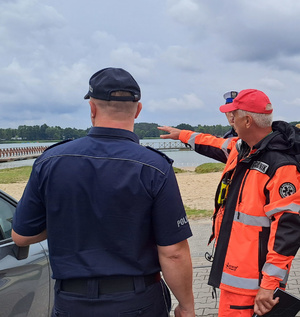 policjant stoi, ratownik wskazuje na jezioro