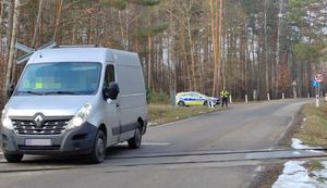 pojazd typu bus koloru szarego przejeżdżający przez tory kolejowe