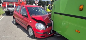 Miejsce wypadku drogowego w Uhrusku. Na zdjęciu widoczny jest zielony autobus, czerwony uszkodzony samochód osobowy po czołowym zderzeniu z autobusem, a w tle wóz straży pożarnej i kierujący ruchem policjant w białej czapce ruchu drogowego