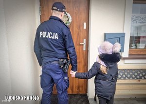 policjant trzyma za rękę dziewczynkę widok z tyłu