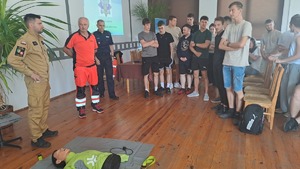 Zdjęcie z debaty społecznej we Włodawie -  trzech prelegentów - przedstawiciel Policji, Ratownictwa Wodnego i Straży Pożarnej. Na podłodze leży manekin na którym będzie prowadzony pokaz pierwszej pomocy. Wokół stoi młodzież uczestnicząca w debacie