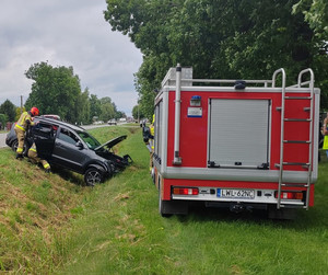 auto w rowie strażacy wykonują przy nim czynności obok wóz strażacki