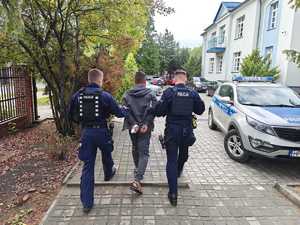 dwóch policjantów doprowadza do pojazdu służbowego tymczasowo aresztowanego 34 latka