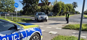Fragment radiowozu policyjnego, policjant ruchu drogowego podczas zatrzymania do kontroli drogowej pojazdu z niesprawnym oświetleniem