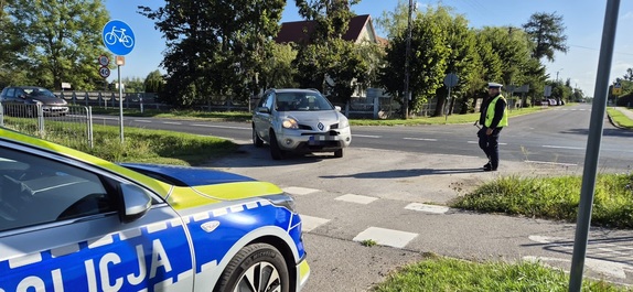 Fragment radiowozu policyjnego, policjant ruchu drogowego podczas zatrzymania do kontroli drogowej pojazdu z niesprawnym oświetleniem