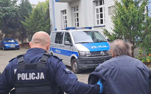 policjant prowadzi zatrzymanego w tle radiowóz