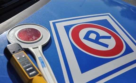 Pokrywa silnika pojazdu policyjnego z symbolem R oznaczającym służbę Ruchu Drogowego, obok leży policyjna biało czerwona tarcza  do zatrzymywania pojazdów i żółte urządzenie do badania stanu trzeźwości