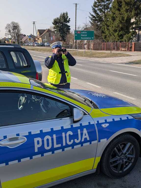 zdjęcie przedstawiające policjanta w trakcie służby wykorzystującego lornetkę w celu sprawdzenia przestrzegania obowiązku korzystania z pasów bezpieczeństwa