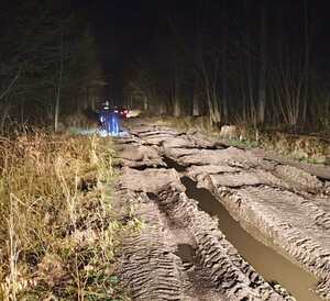 Zdjęcia z lasu w którym wraz z dziećmi zgubiła się 47-latka - grząska droga leśna, idąca pieszo dwójka policjantów, w tle samochód