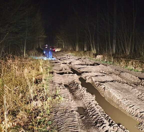 Zdjęcia z lasu w którym wraz z dziećmi zgubiła się 47-latka - grząska droga leśna, idąca pieszo dwójka policjantów, w tle samochód