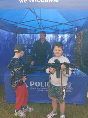 zdjęcie przedstawia policyjne stoisko. Widoczny jest policjant oraz dwoje dzieci, jedno ogląda broń