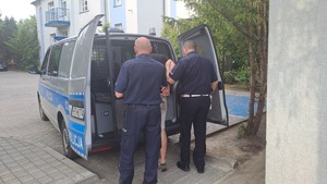 Dwóch policjantów doprowadza do radiowozu tymczasowo aresztowanego 23 latka, który znęcał się nad rodziną.
