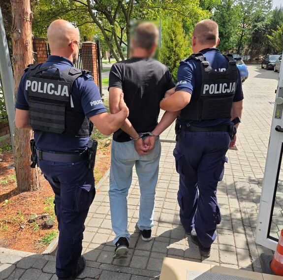 Zdjęcie przedstawia mężczyznę podejrzanego o stalking podczas doprowadzania do sądu prze dwóch funkcjonariuszy policji